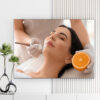 Mẫu tranh spa đẹp hình ảnh nhân viên đang bôi kem dưỡng da mặt cho nữ khách hàng và miếng cam chín vàng