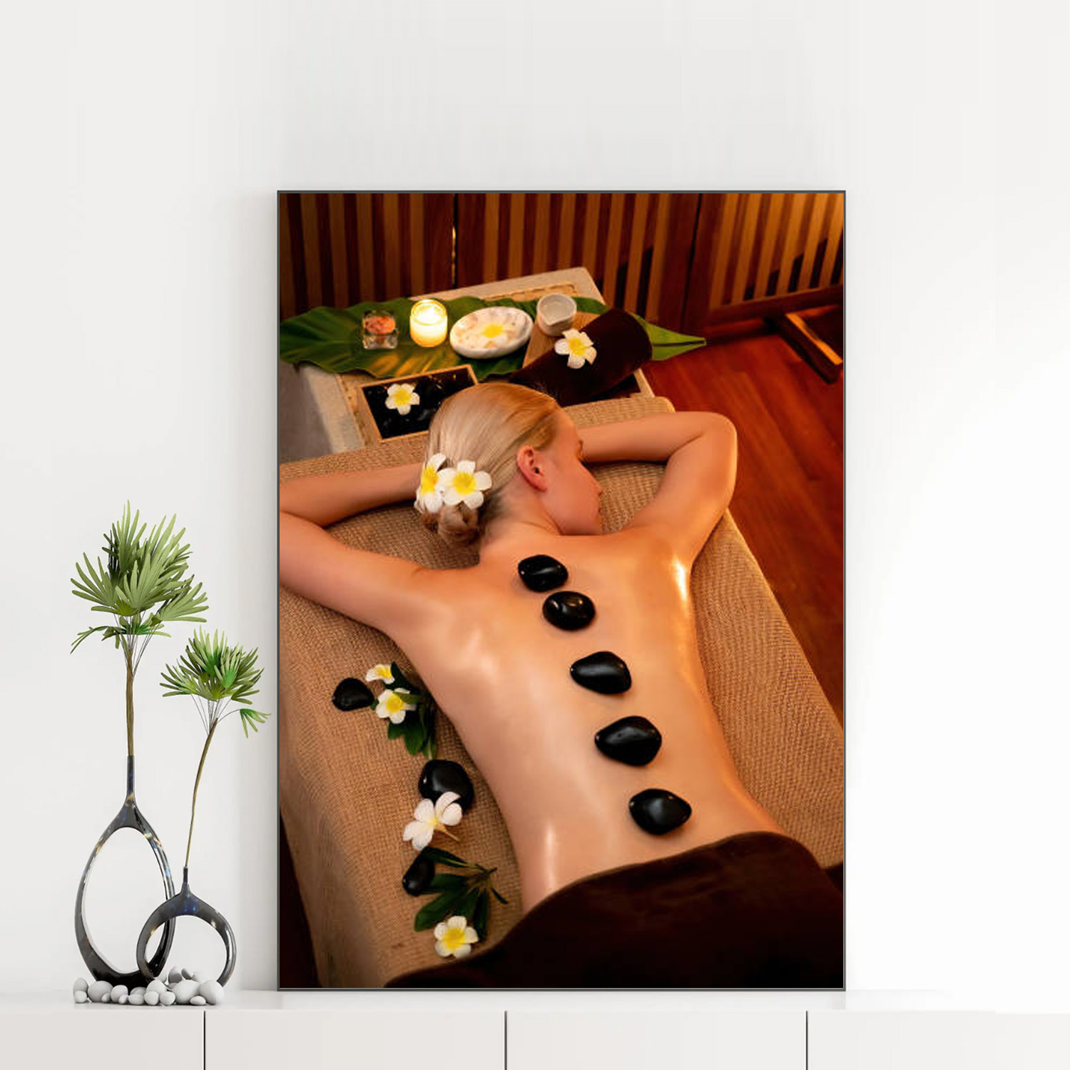 Mẫu tranh spa đẹp khổ đứng hình ảnh cô gái nằm thư giãn trong phòng spa với hàng đá cuội nóng chườm trên lưng, xung quanh trang trí hoa sứ trắng và nến thơm